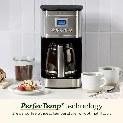 Coffee maker with carafe, cups, and pastries on a kitchen counter.