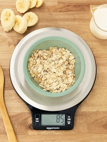 Oats in a bowl on a digital scale with bananas and milk nearby.