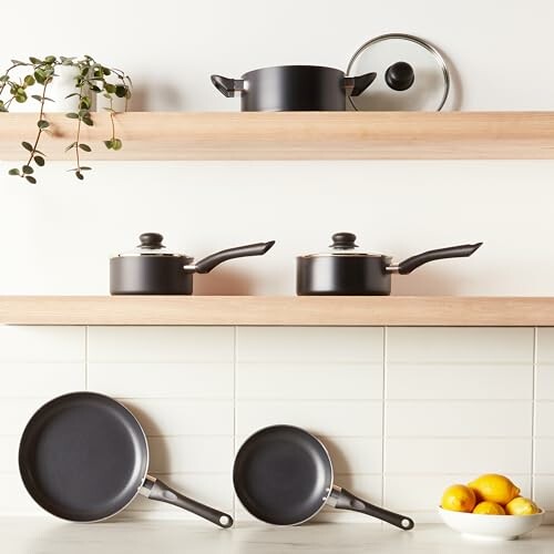 Cookware including pots and pans on kitchen shelves with lemons.
